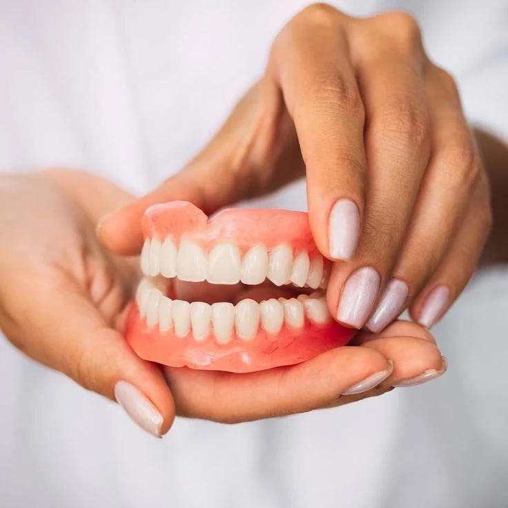 fingers holding plastic dentures with teeth in palm of hand in belmont sutton