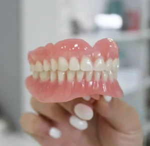 complete dentures plastic dentures woman holding dentures with fingers white smile white teeth dentist in belmont sutton